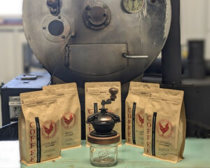 Bags of Red Rooster small batch coffee with the Camano Coffee Mill manual coffee grinder in front of the coffee roaster